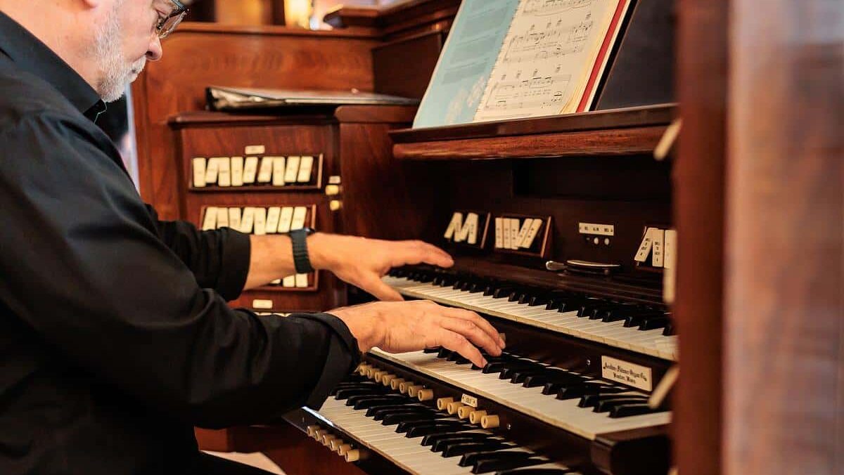 a man with hands resting on a pipe organ keys.