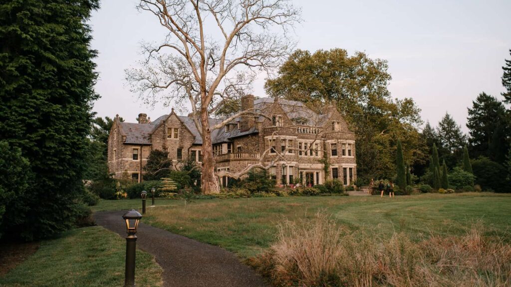 alt text: A large manor house and the silhouette of a tree in front of a large lawn.