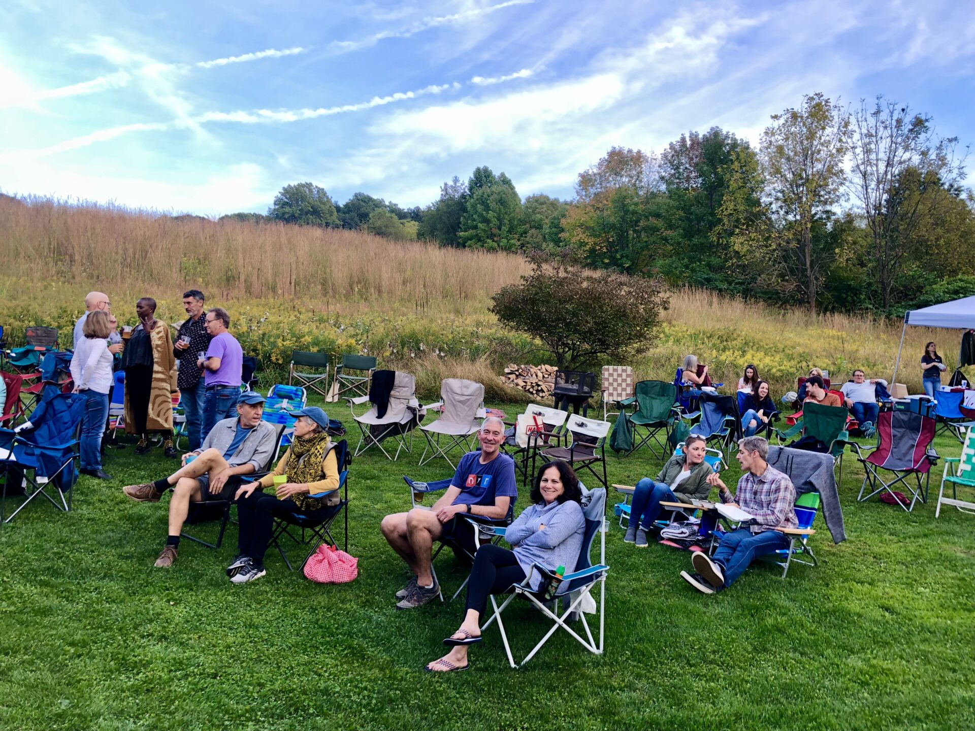 people sitting in lawn chairs on green grass with a meadow and trees in the background