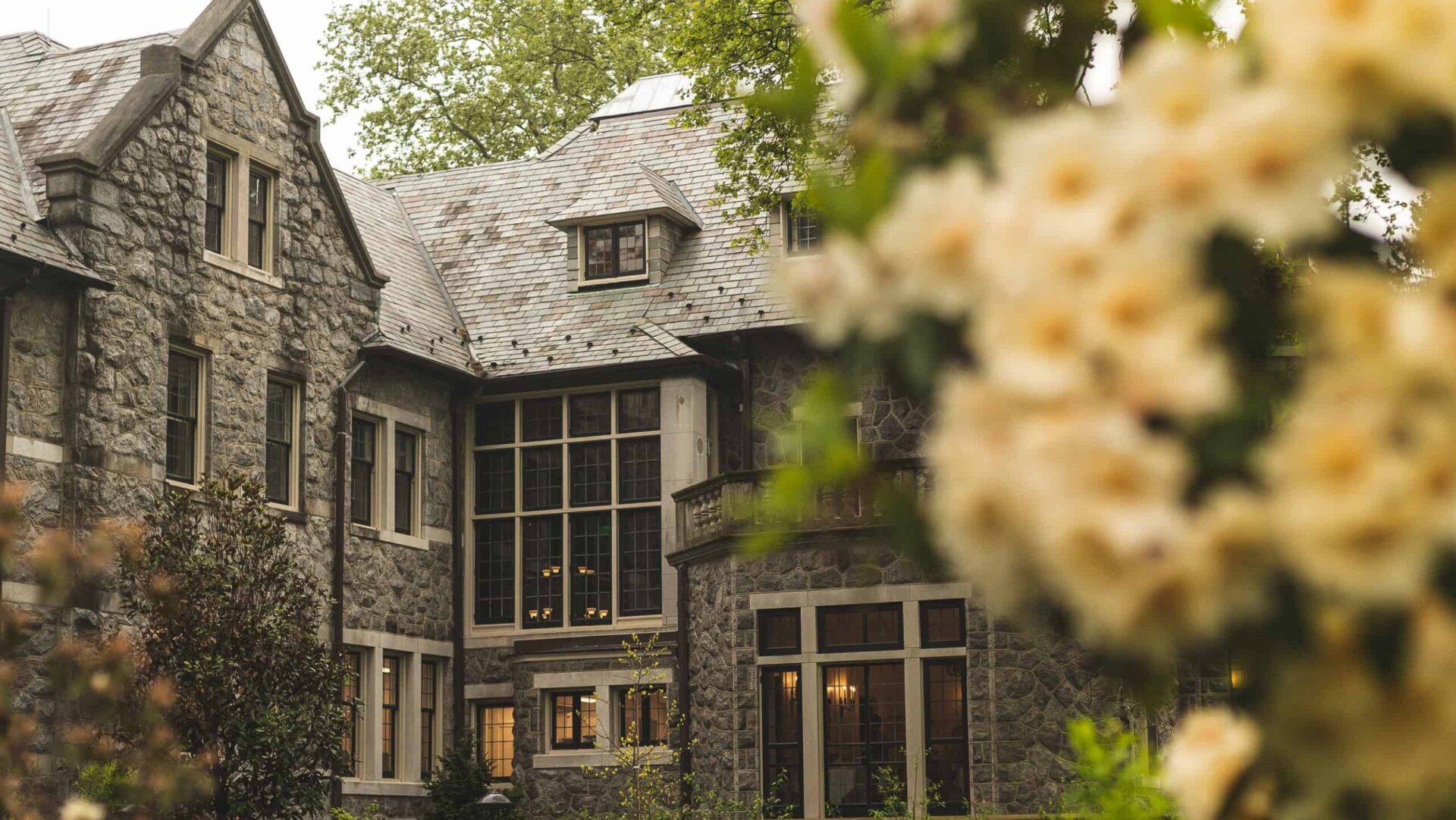 Stoneleigh Stroll About – Photos by Adam HribarMay 13 A large stone mansion with pale yellow azaleas blooming under foggy