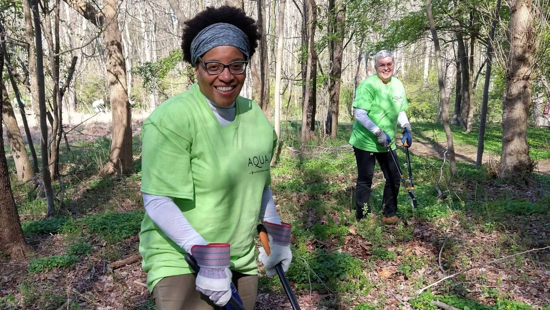 Two women with Aqua company shirts on prune invasive vines in a forest.