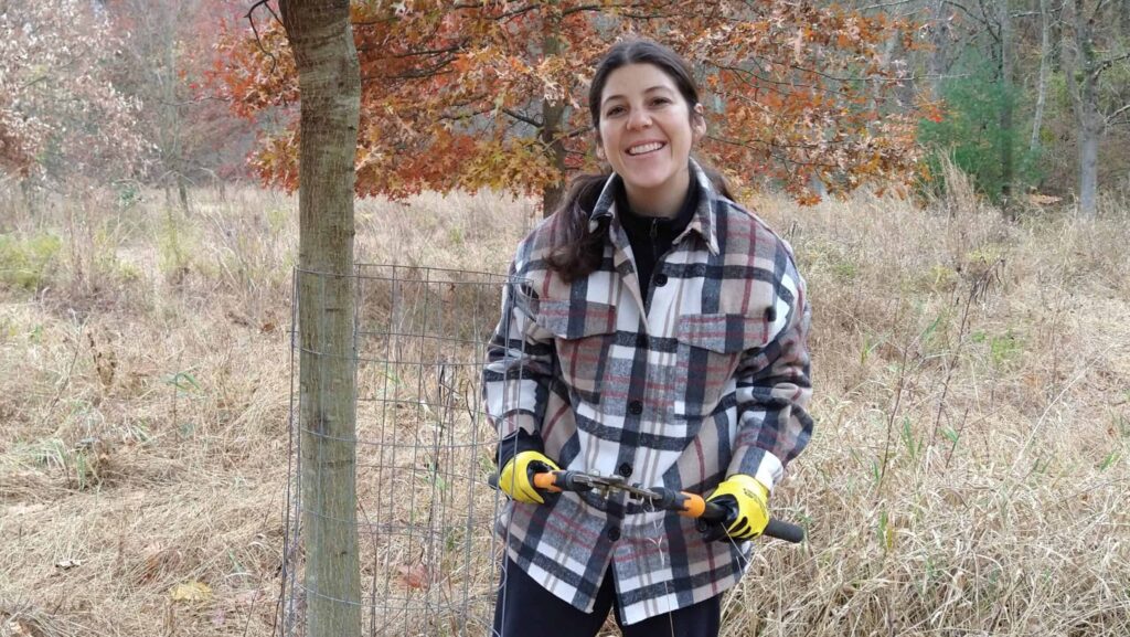 Smiling woman standing next to a tree holding loppers.
