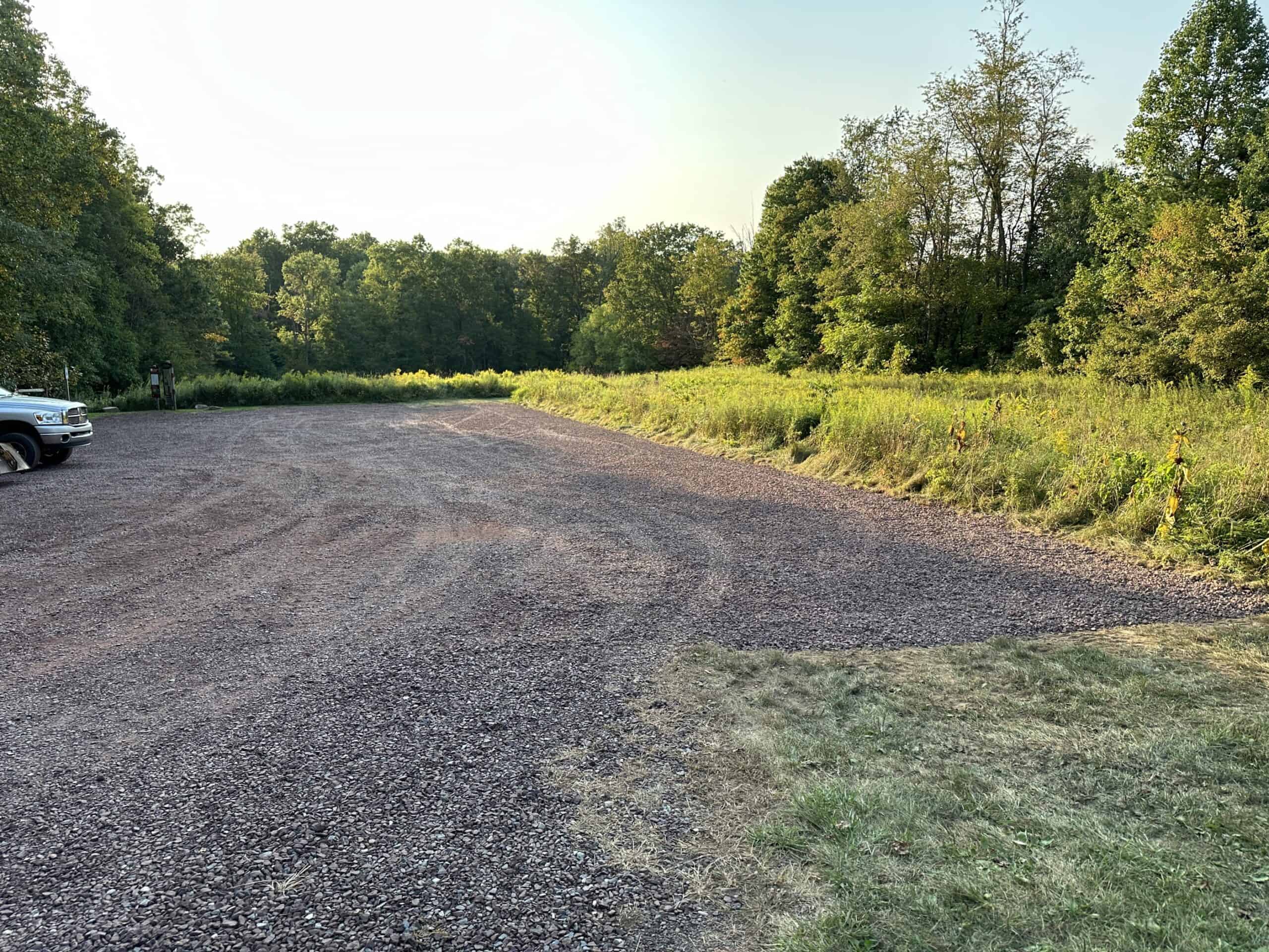 Gravel parking lot surrounded by meadow and woods.