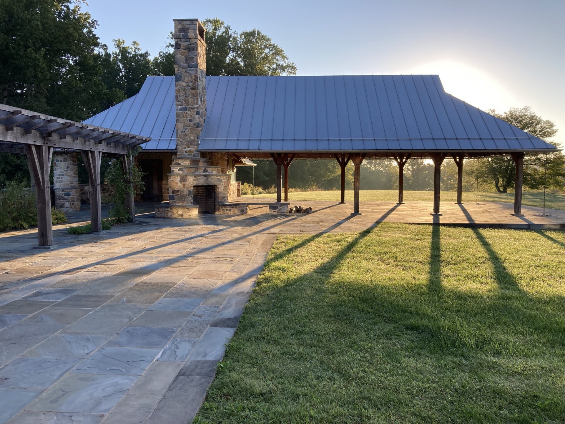 sun shining through an outdoor pavilion with arbor and stone patio