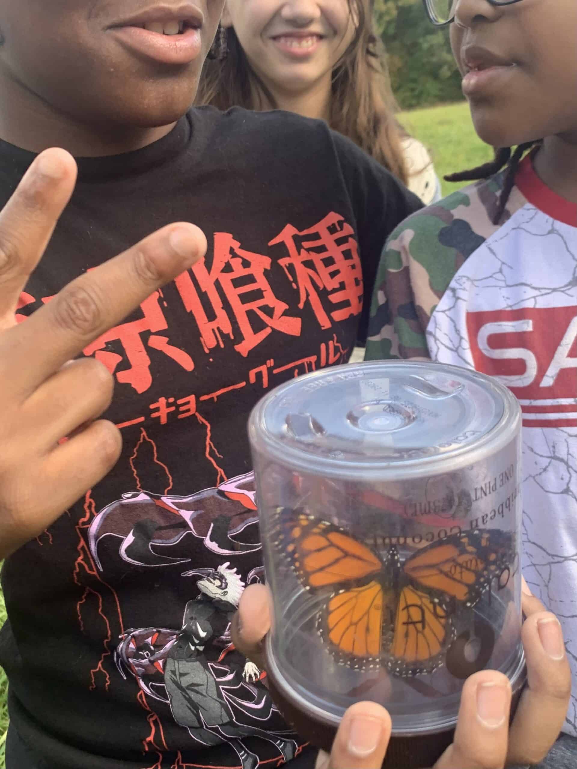 Students holding a Monarch butterfly in a container.