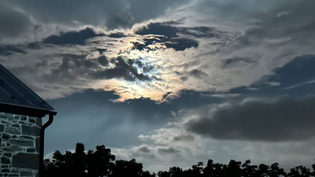 The moon behind the clouds in a spooky image.