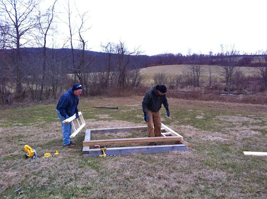 two men building a wooden shed outside in a field