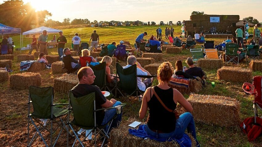 people sitting in a field during golden hour with a band playing on a stage in the background