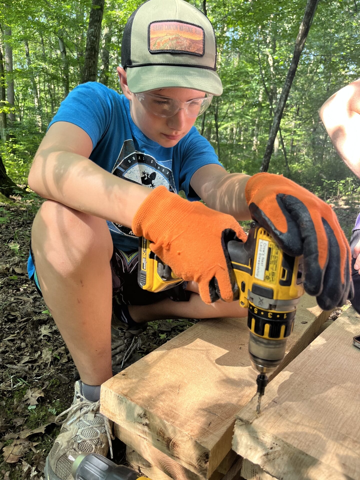 A summer camper uses a cordless drill to prepare boardwalk planks.