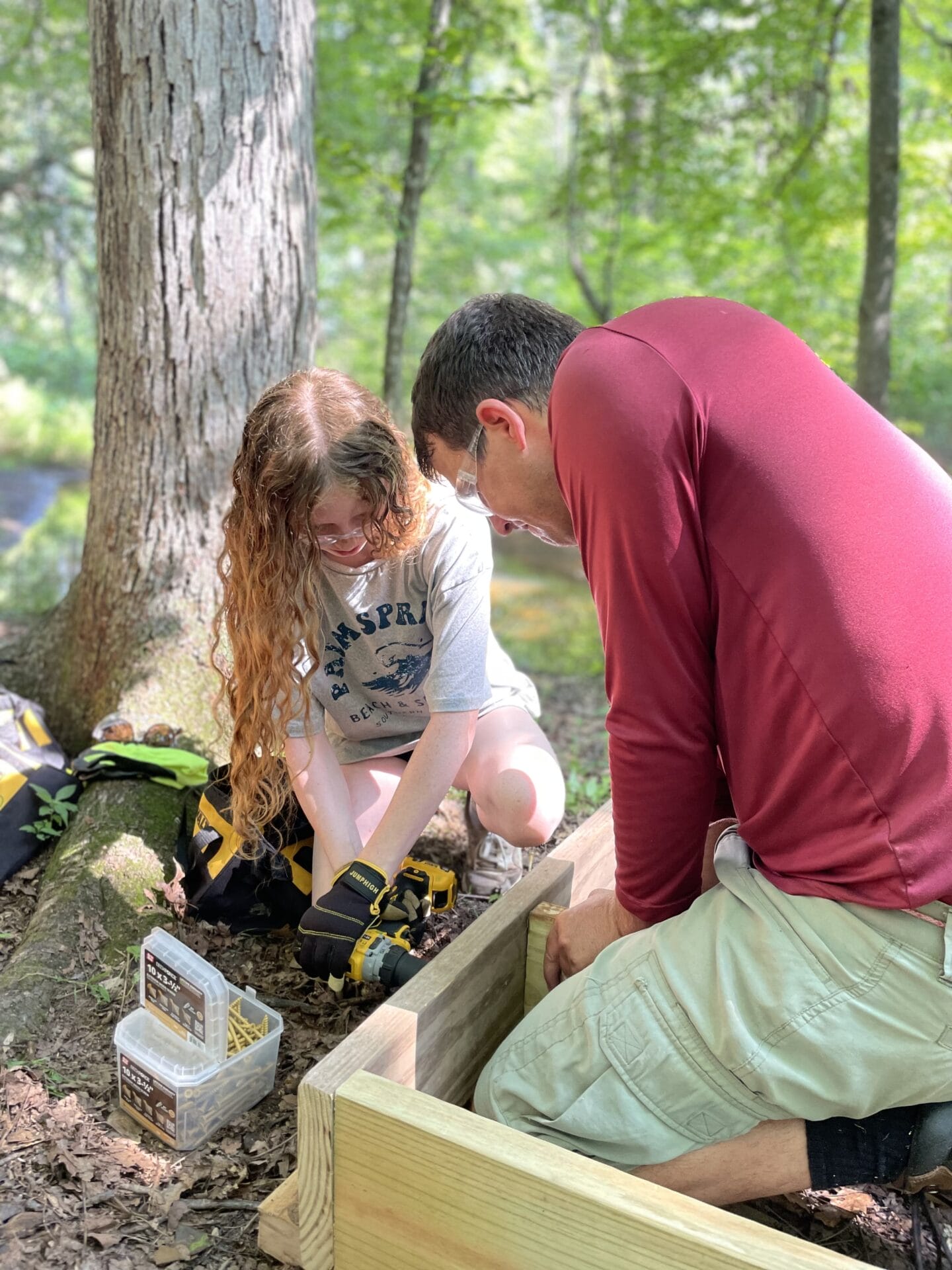 A camp counselor assists a camper build a footbridge.