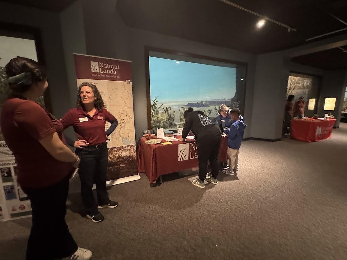 outreach table set up in the Academy of Natural Sciences with staff members interacting with visitors at the table