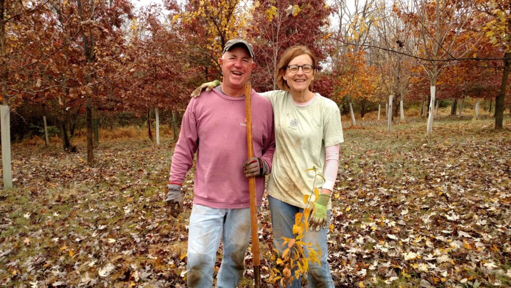 a man and woman smiling while planting a shrub