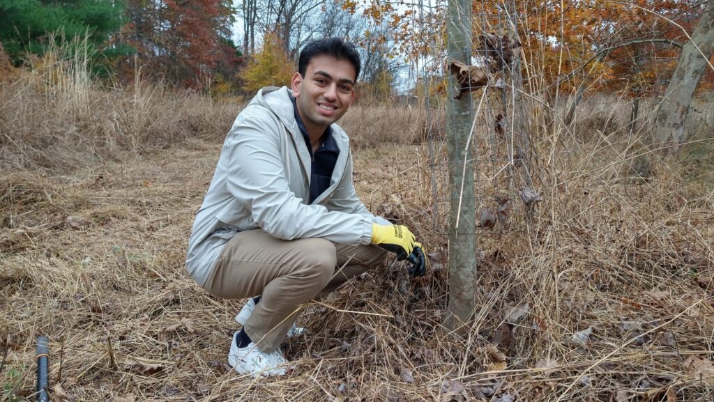 a smiling man crouched down with his gloved hands on a tree cage