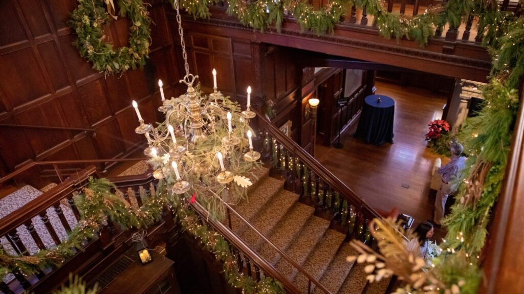 looking down at a chandelier and grand staircase with natural holiday decor around