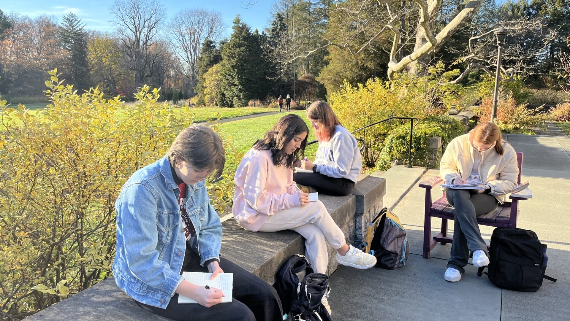 students sitting on a porch in a garden writing in notebooks