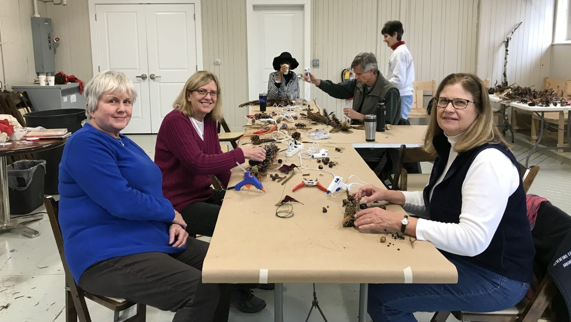 volunteers sitting around a tabling smiling and working on natural holiday decor