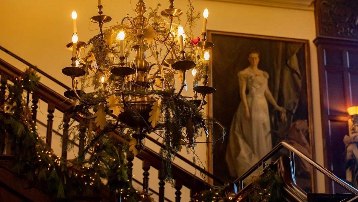 Home For the Holidays 2023 Home for the Holidays 2023 a chandelier and staircase decorated in holiday decor with a portrait painting in the background