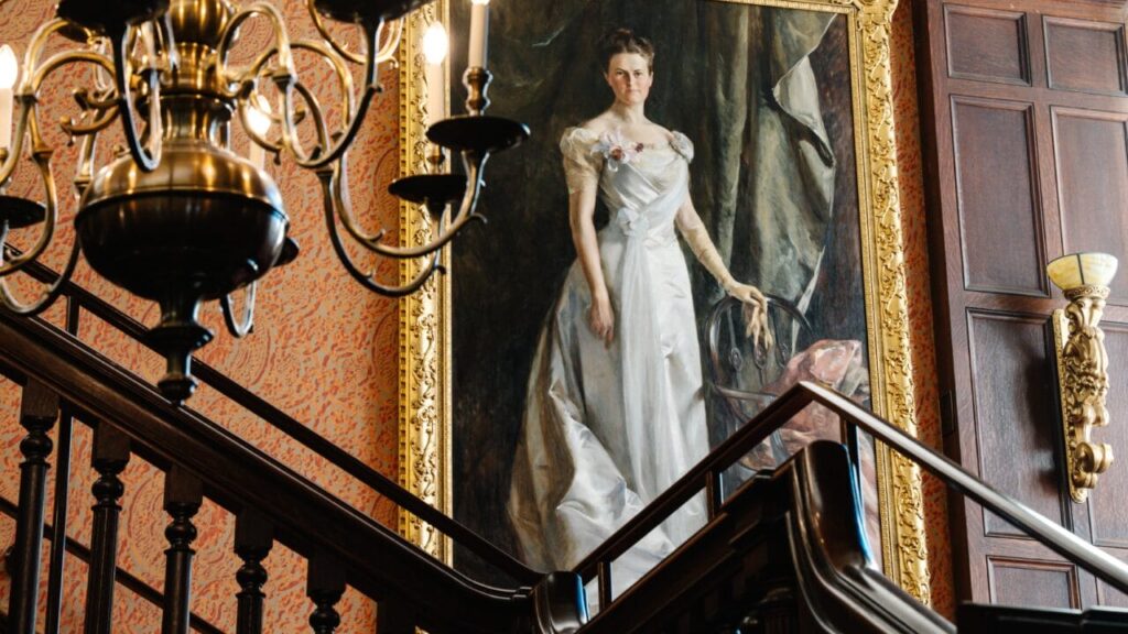 grand staircase with a chandelier and victorian painting of a woman