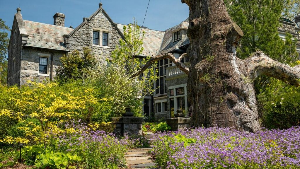 a stone mansion surrounded by gardens with purple and yellow flowers