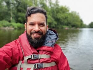 A man in a red jacket and life vest with water behind