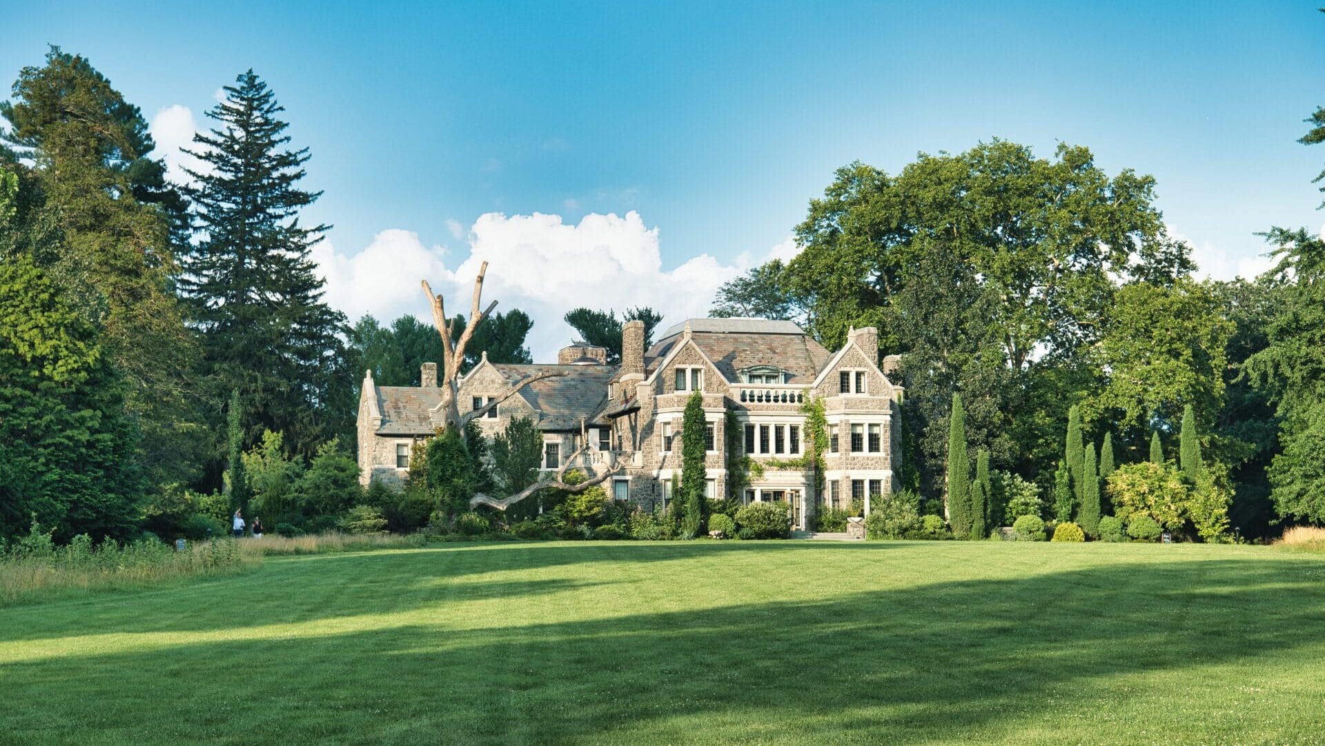 view of a victorian stone house surrounded by trees from a green lawn