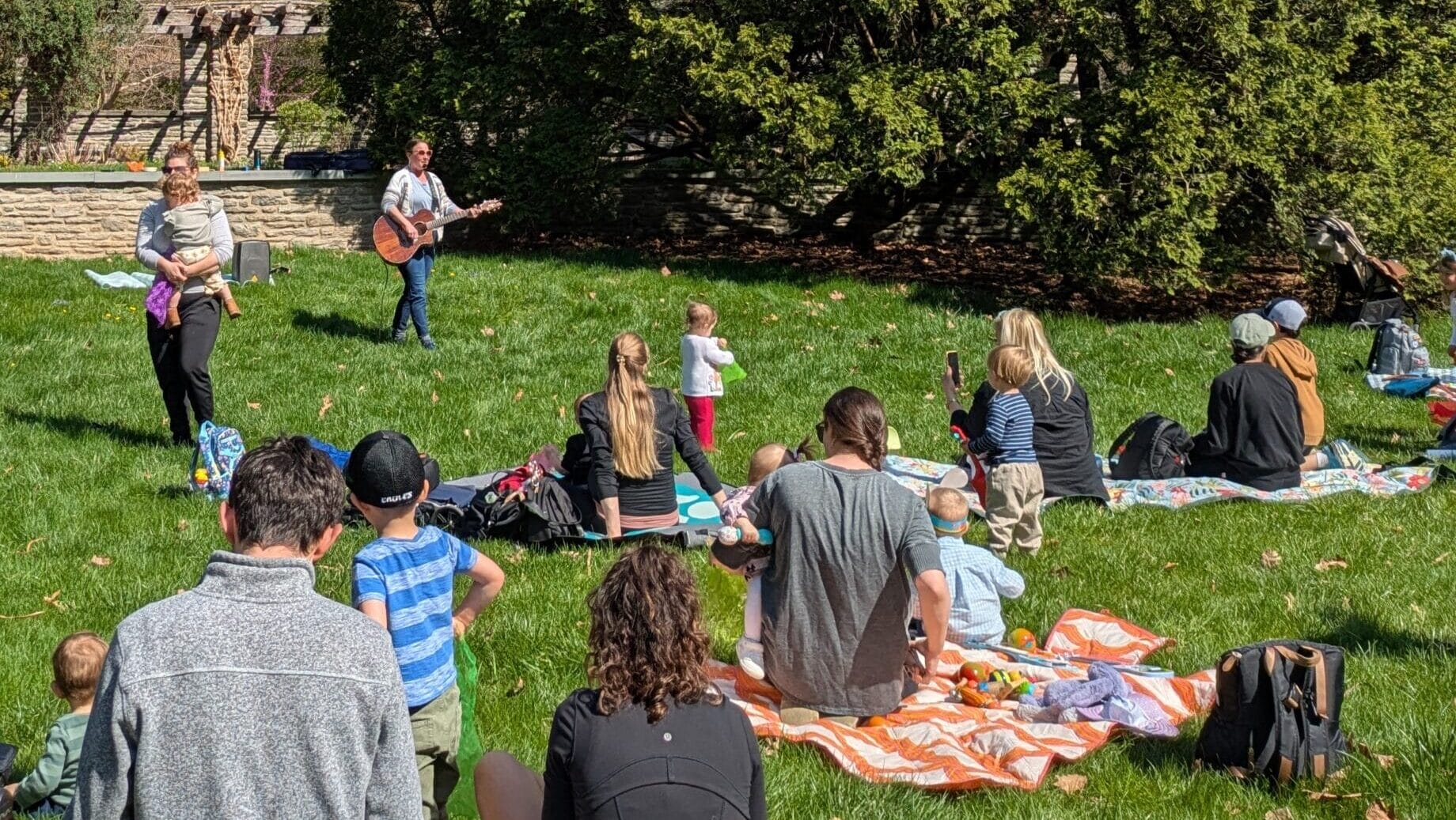 parents with their children in a garden watching a musician