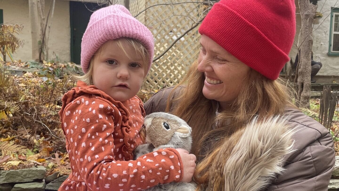 A woman and child with a stuffed animal outdoors.