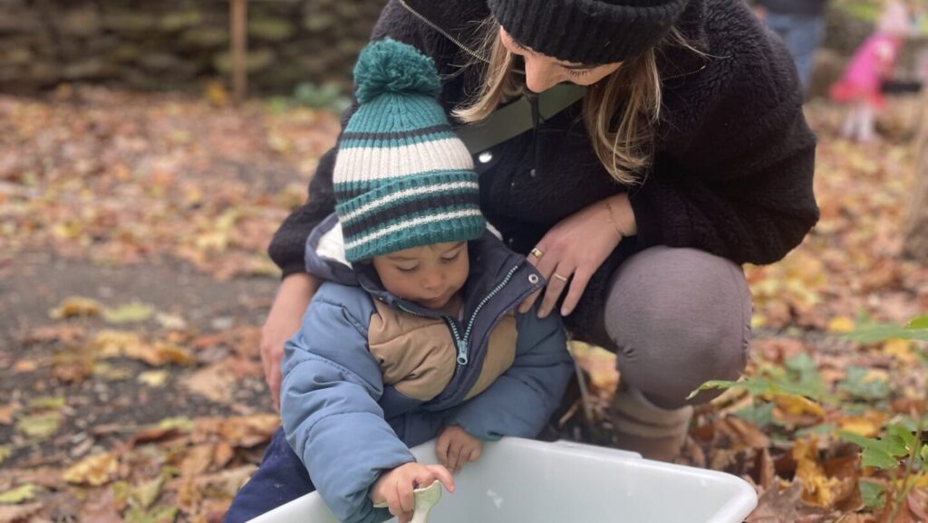 A woman and child outdoors playing in a bin with a toy.