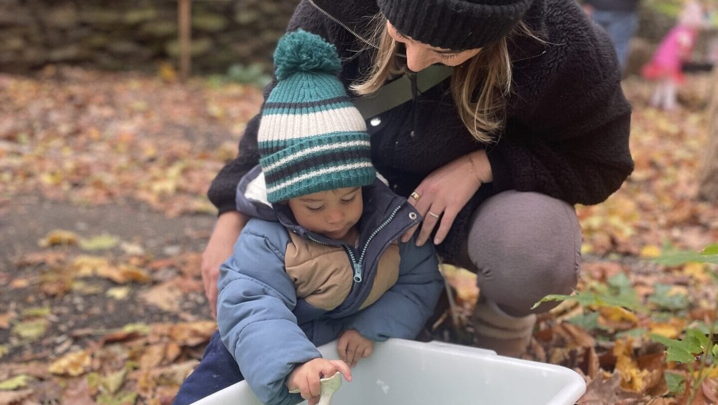 A woman and child outdoors playing in a bin with a toy.