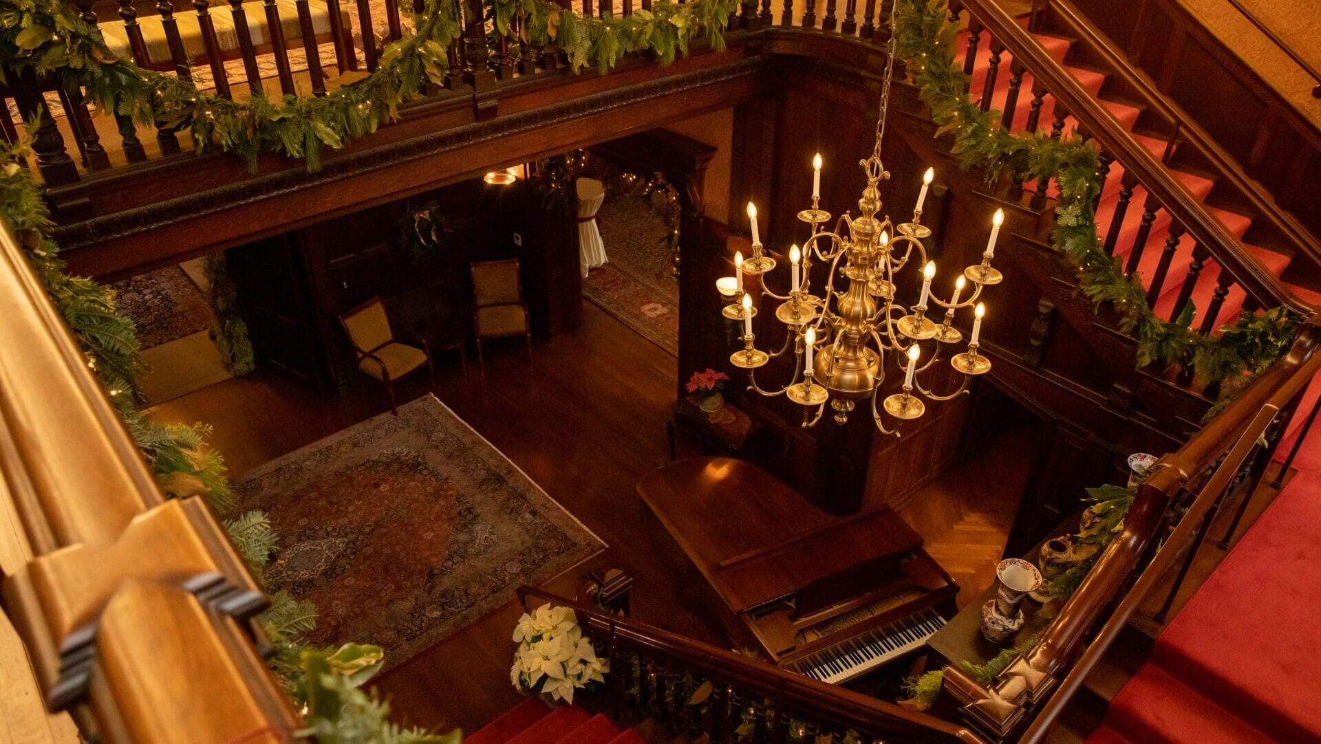 A view looking down of a chandelier, stairs, and a piano.