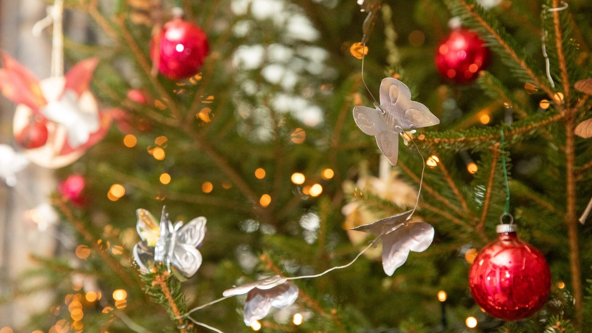 Red ornaments and metal butterfly garland on a Christmas tree.