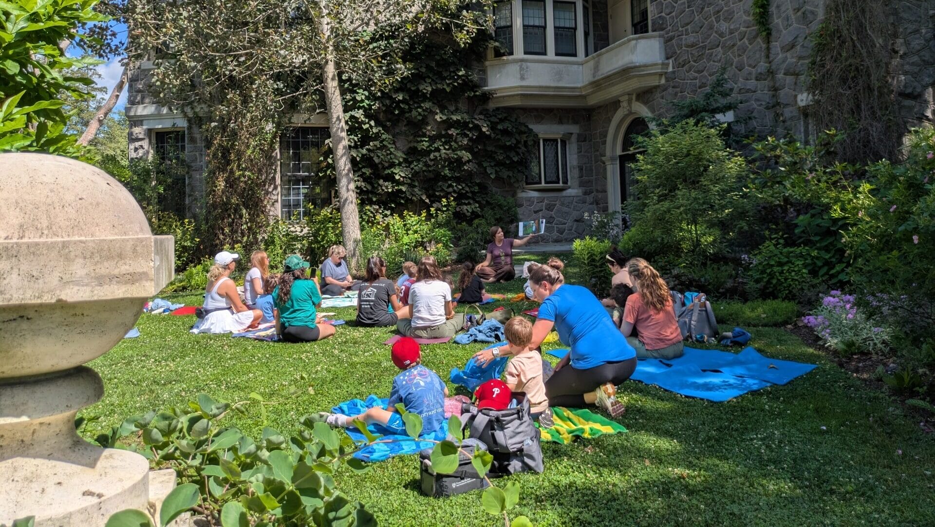 Women and children on yoga mats with a woman reading and showing a book.